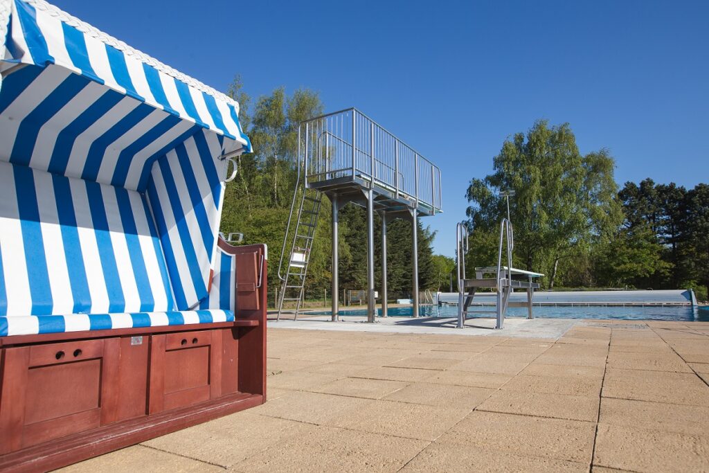 Im Vordergrund steht ein Strandkorb und im Hintergrund der 3 Meter und der 1 Meter Sprungturm.